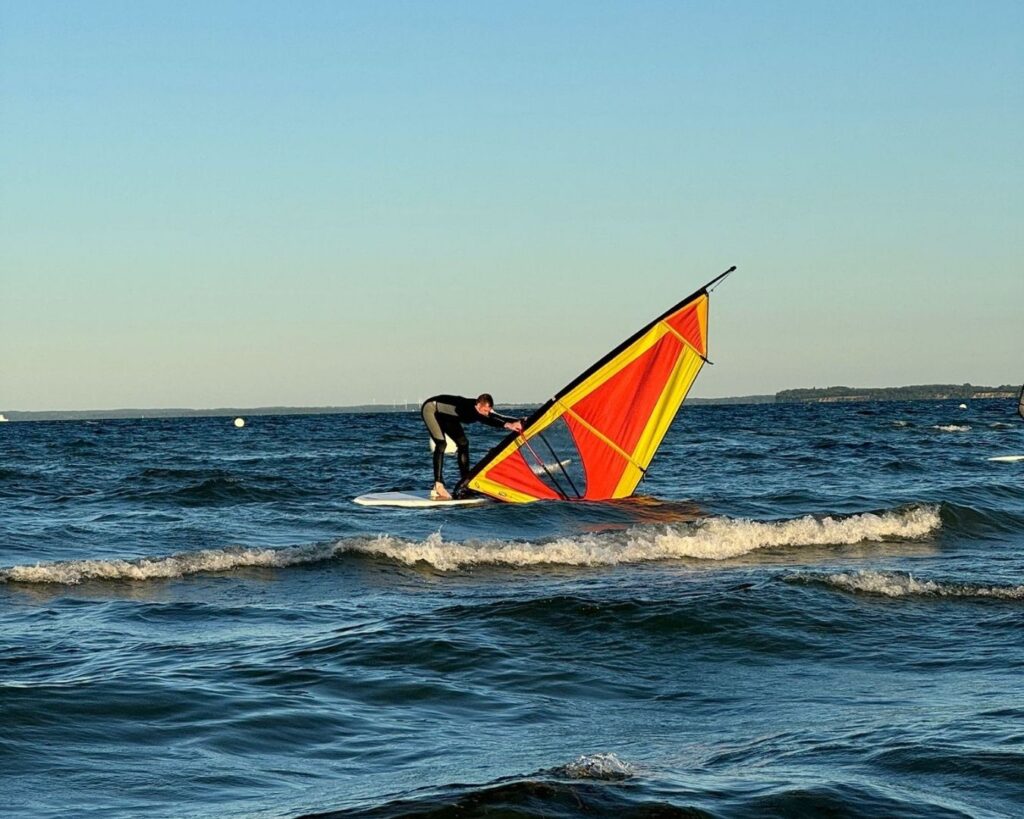 Schüler beim Üben Windsurfen auf dem Wasser mit dem Segel in der Hand